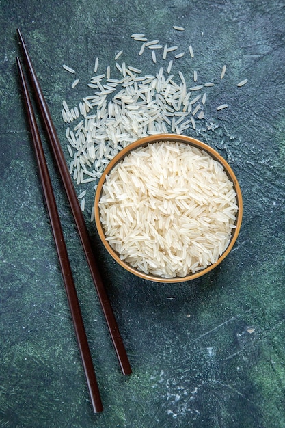 Photo gratuite vue de dessus du riz cru avec des bâtonnets à l'intérieur de la plaque sur un bureau sombre