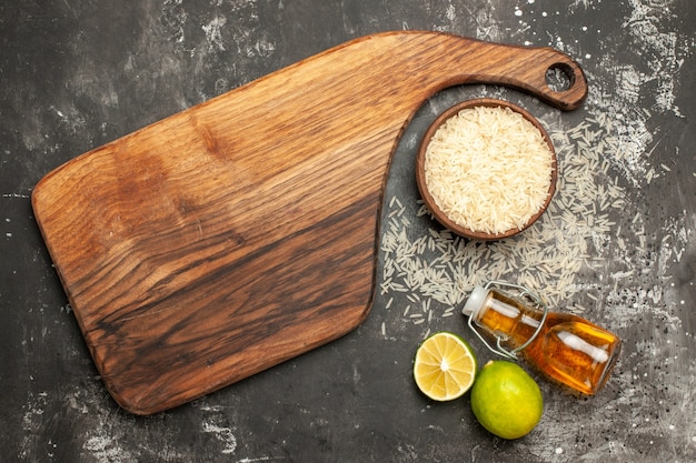 Photo gratuite vue de dessus du riz cru avec des citrons et de l'huile sur la couleur des fruits des aliments crus de surface sombre