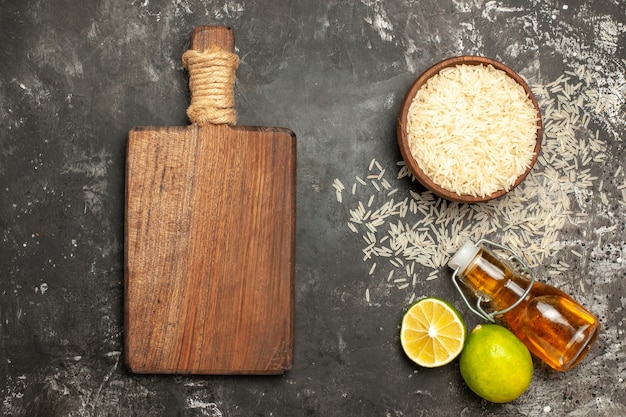 Photo gratuite vue de dessus du riz cru avec des citrons et de l'huile sur une surface sombre de l'huile alimentaire crue