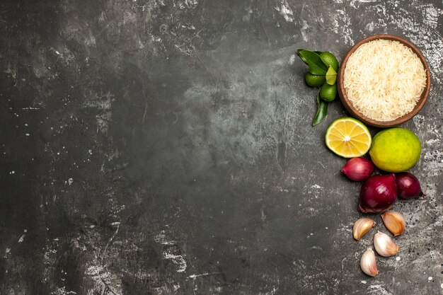 Vue de dessus du riz cru avec des oignons et de l'ail sur la salade mûre d'aliments crus de surface sombre