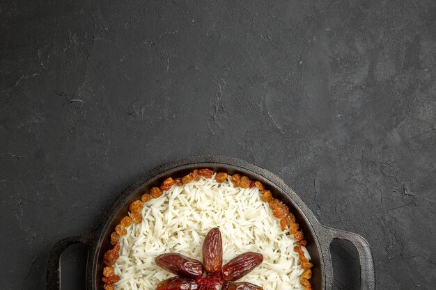 Vue de dessus du riz cuit avec des raisins secs à l'intérieur de la casserole sur une surface sombre riz alimentaire repas oriental dîner