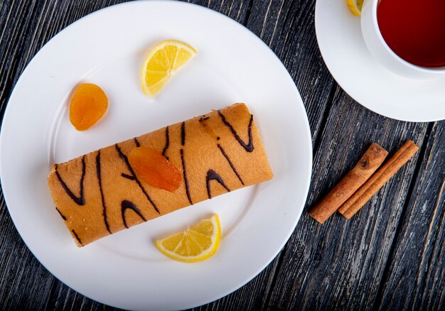 Vue de dessus du rouleau suisse avec de la confiture d'abricot sur une plaque blanche servie avec une tasse de thé sur rustique