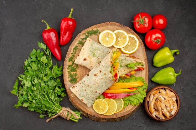 Vue de dessus du sandwich à la viande de shaurma en tranches avec des tranches de citron et des verts sur fond noir