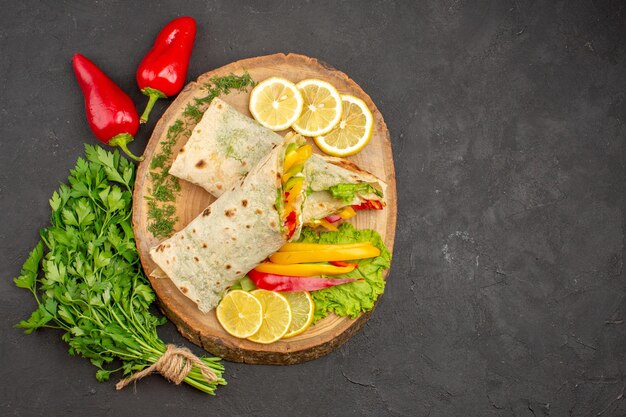 Vue de dessus du sandwich à la viande de shaurma en tranches avec des verts de citron sur fond noir