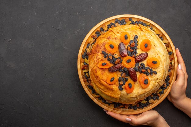 Vue de dessus du savoureux riz cuit shakh plov à l'intérieur d'une pâte ronde avec des raisins secs sur une surface grise