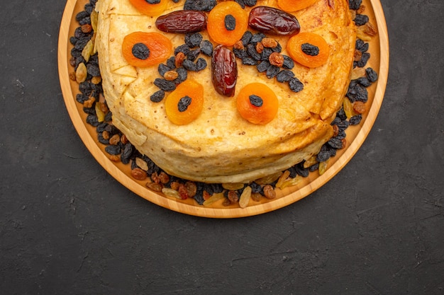 Vue de dessus du savoureux riz cuit shakh plov à l'intérieur d'une pâte ronde avec des raisins secs sur une surface grise