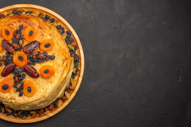 Vue de dessus du savoureux riz cuit shakh plov à l'intérieur d'une pâte ronde avec des raisins secs sur une surface grise