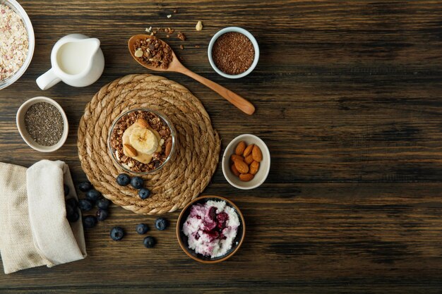 Vue de dessus du smoothie à la banane amande lait de noix beurre de cacahuète sur dessous de plat avec cuillerée de noix fromage cottage avoine sésame prunellier débordant de sac sur fond en bois avec espace de copie