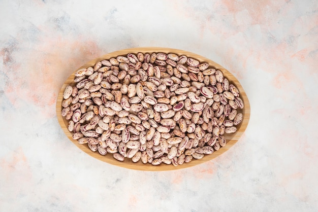 Photo gratuite vue de dessus du tas de haricots dans une assiette en bois sur une table blanche.