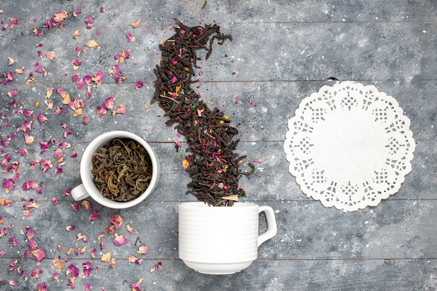 Photo gratuite vue de dessus du thé séché frais à l'intérieur et à l'extérieur de la tasse sur le bureau rustique gris