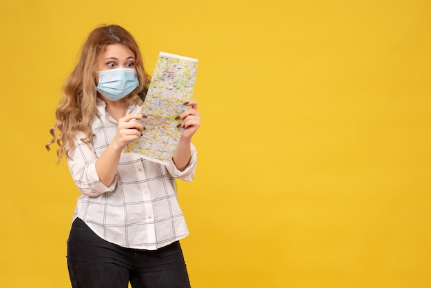 Vue de dessus du voyage fille portant son masque et sac à dos en regardant la carte sur jaune