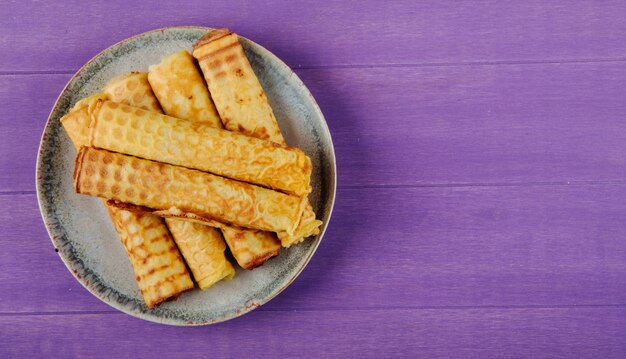 Vue de dessus du wafer roll rempli de lait concentré sur une plaque sur fond violet en bois avec copie espace