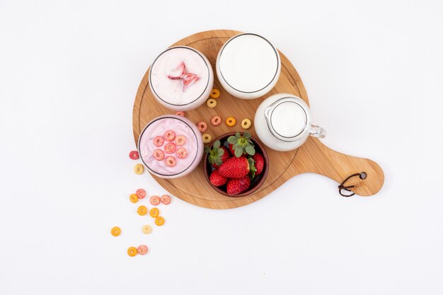 Vue de dessus du yaourt au lait et aux fraises sur une planche à découper en bois sur une surface blanche horizontale