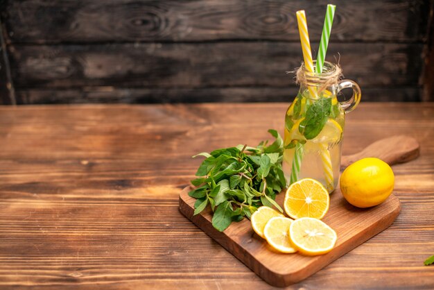 Vue de dessus de l'eau de désintoxication fraîche naturelle servie avec des tubes menthe et orange sur le côté gauche sur une table en bois