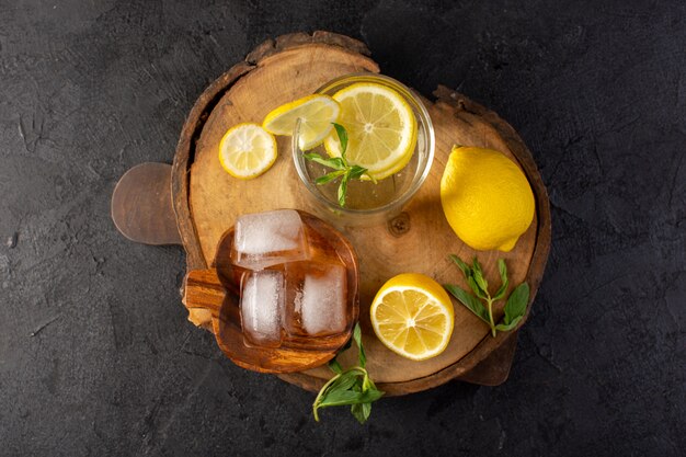 Une vue de dessus de l'eau avec du citron boisson fraîche fraîche à l'intérieur du verre avec des glaçons avec des citrons en tranches sur le fond sombre boisson cocktail fruit
