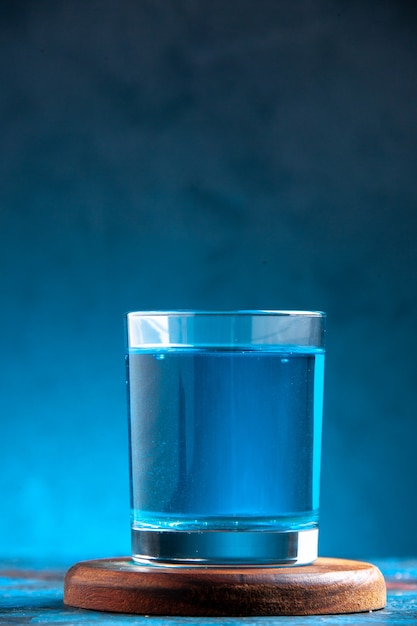 Vue de dessus d'une eau plate dans un verre sur une planche à découper en bois sur fond bleu