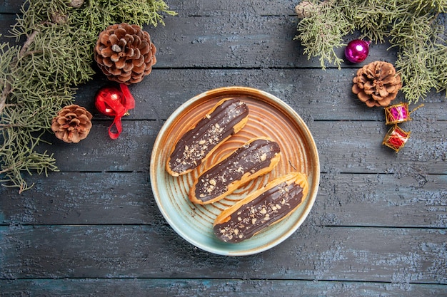 Vue de dessus éclairs au chocolat sur plaque ovale pommes de pin jouets de Noël sapin feuilles sur table en bois foncé avec espace libre