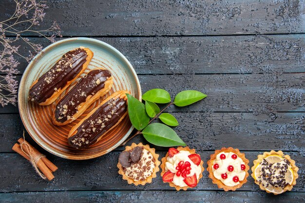 Vue de dessus éclairs au chocolat sur plaque ovale tartes cannelle et laeves sur la table en bois foncé avec espace copie