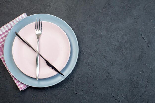 Vue de dessus élégante assiette rose avec couteau et fourchette à assiette bleue sur une surface sombre