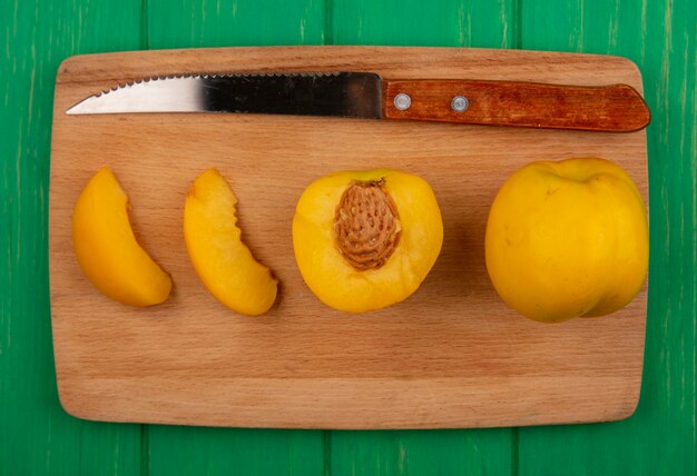 Vue de dessus de l'ensemble des abricots coupés et tranchés avec un couteau sur une planche à découper sur fond vert