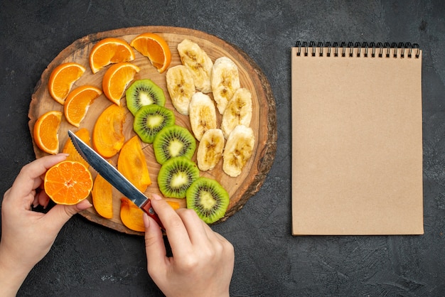 Photo gratuite vue de dessus d'un ensemble de fruits frais biologiques naturels sur une planche à découper et un cahier à spirale sur fond sombre