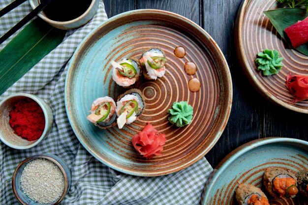 Vue de dessus de l'ensemble de rouleaux de sushi cuit au four avec des crevettes servi avec du wasabi et du gingembre sur une assiette sur bois