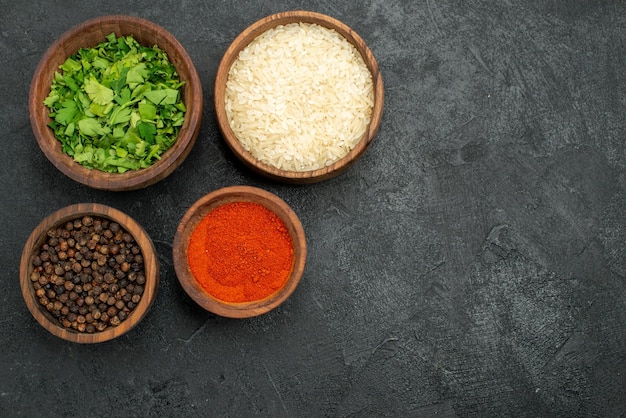 Vue de dessus épices dans des bols herbes de pavot noir épices colorées et riz sur le côté gauche de la table sombre