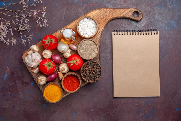 Photo gratuite vue de dessus épices sur la planche épices tomates oignons champignons et une bouteille d'huile sur la planche à découper et un cahier