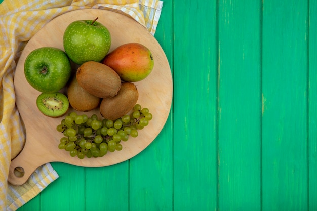 Vue de dessus espace copie pommes vertes avec raisins verts kiwi et poire sur un support avec une serviette à carreaux jaune sur fond vert