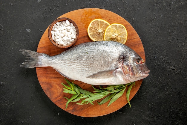 Vue de dessus estragon poisson de mer cru sel de mer dans un bol tranches de citron sur planche de bois ronde sur fond noir