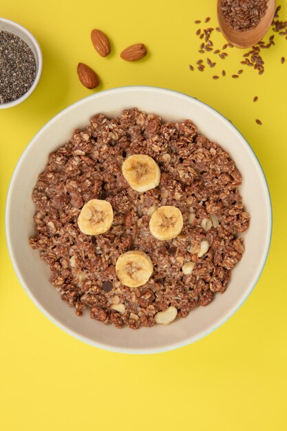 Vue de dessus de la farine d'avoine avec noix de banane dans un bol avec sésame aux amandes sur fond jaune