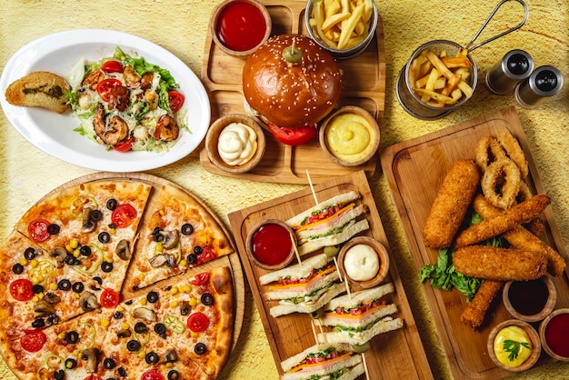 Photo gratuite vue de dessus fast food mix bâtonnets de mozzarella club sandwich hamburger pizza aux champignons pizza césar salade de crevettes frites ketchup mayo et sauces au fromage sur la table