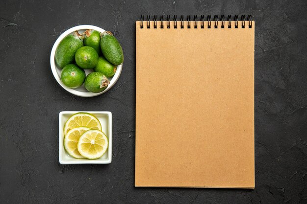Vue de dessus feijoa vert frais avec des tranches de citron et un bloc-notes sur une surface sombre fruit légume agrumes moelleux arbre plante