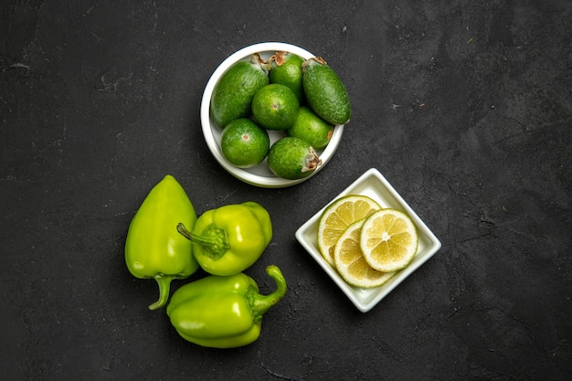 Photo gratuite vue de dessus feijoa vert frais avec des tranches de citron et du poivron vert sur une surface sombre fruit légume agrumes moelleux arbre plante