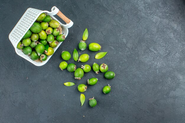 Vue de dessus des feijoas frais dispersés dans un panier en plastique sur une surface sombre avec copie espace