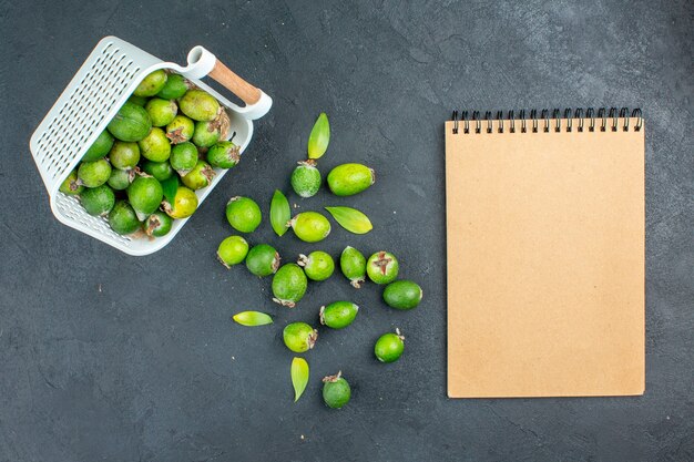 Vue de dessus des feijoas frais dispersés à partir de cahier de panier en plastique sur une surface sombre