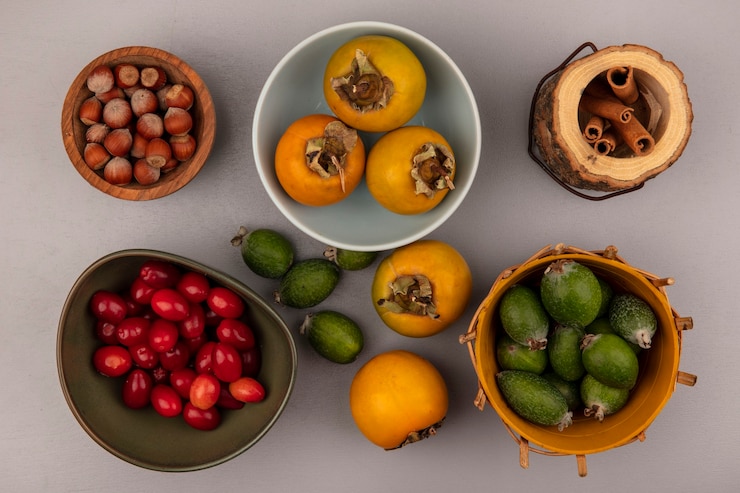 Photo gratuit vue de dessus des feijoas sur un seau avec des kakis sur un bol avec des cerises de cornaline sur un bol avec des noisettes sur un bol en bois avec des bâtons de cannelle sur un mur gris