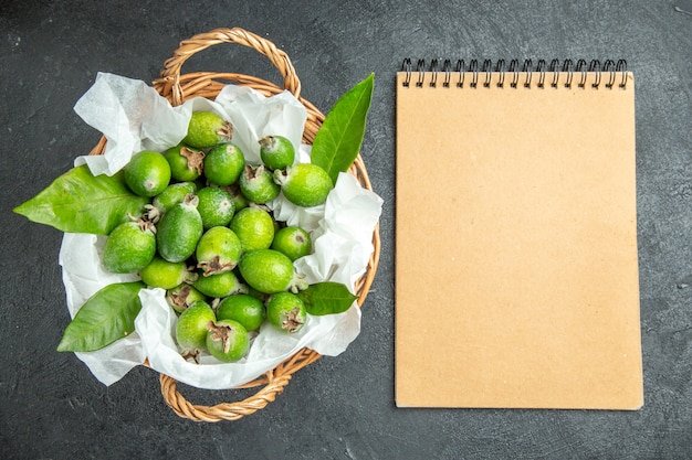 Photo gratuite vue de dessus des feijoas vertes fraîches naturelles avec des feuilles dans un panier et un ordinateur portable tordus marron