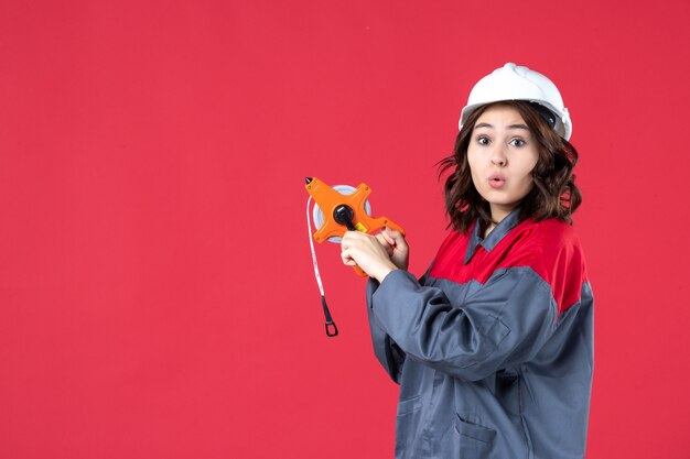 Vue de dessus d'une femme architecte surprise en uniforme avec un casque tenant un ruban à mesurer sur fond rouge isolé