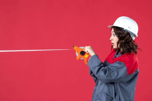 Vue de dessus d'une femme architecte surprise en uniforme avec un ruban à mesurer d'ouverture de casque sur fond rouge isolé