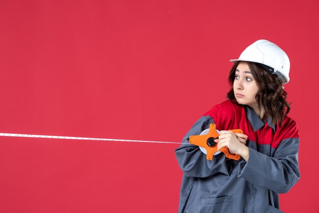 Vue de dessus d'une femme architecte surprise en uniforme avec un ruban à mesurer d'ouverture de casque regardant en arrière sur fond rouge isolé