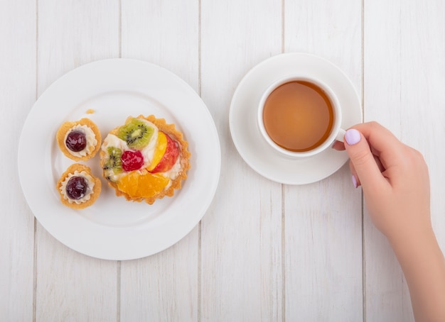 Vue de dessus femme buvant une tasse de thé avec des tartelettes sur plaque sur fond blanc