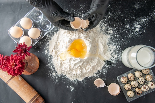 Vue de dessus femme cuisinier casser les œufs en farine sur une surface sombre