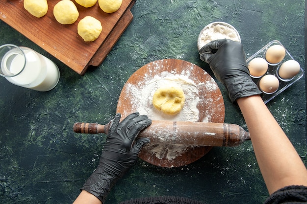 Vue de dessus femme cuisinière étalant la pâte avec de la farine sur une surface sombre