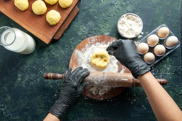 Vue de dessus femme cuisinière étalant la pâte avec de la farine sur une surface sombre