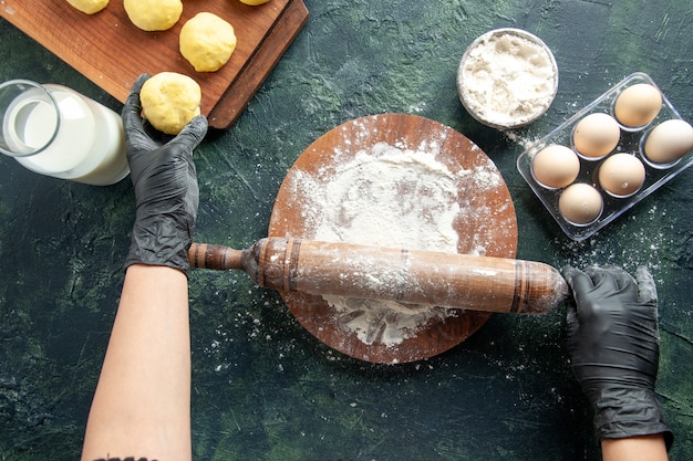 Vue de dessus femme cuisinière étalant la pâte avec de la farine sur une surface sombre