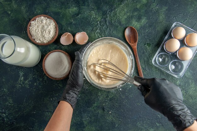 Vue de dessus femme cuisinière mélangeant de la farine dans une assiette avec des œufs sur une surface sombre