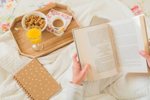 Vue de dessus de la femme avec un livre ouvert et plateau de petit déjeuner