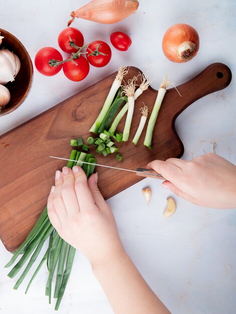 Vue de dessus de femme main couper l'oignon sur une planche à découper et tomates sur fond blanc