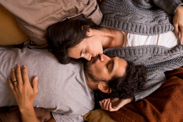 Vue de dessus femme et mari s'embrassant en position couchée dans son lit